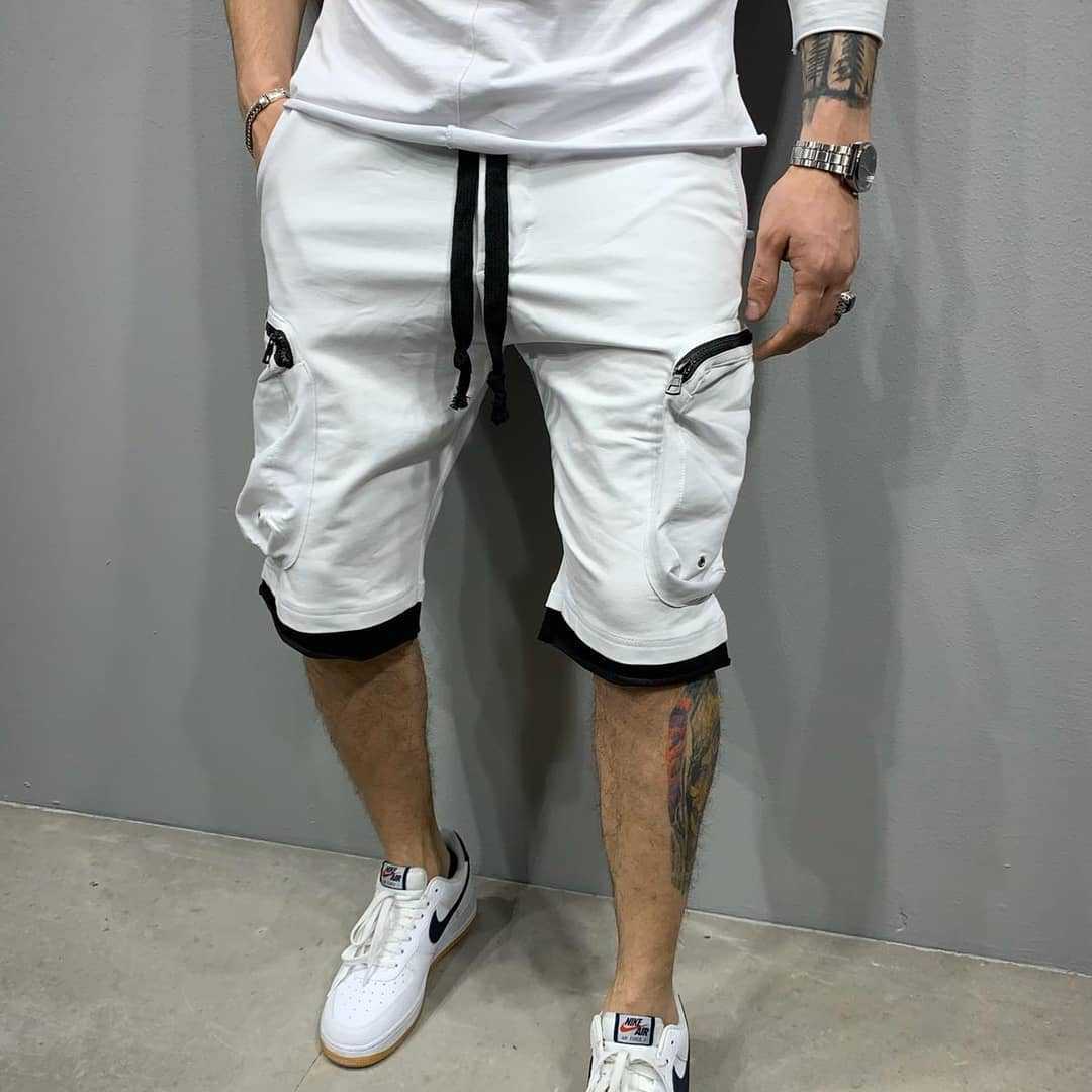 Person wearing white shorts with black accents and white sneakers against a gray background